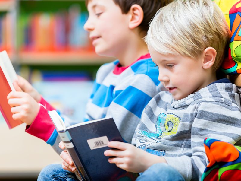 To drenge læser hver deres bog på et bibliotek